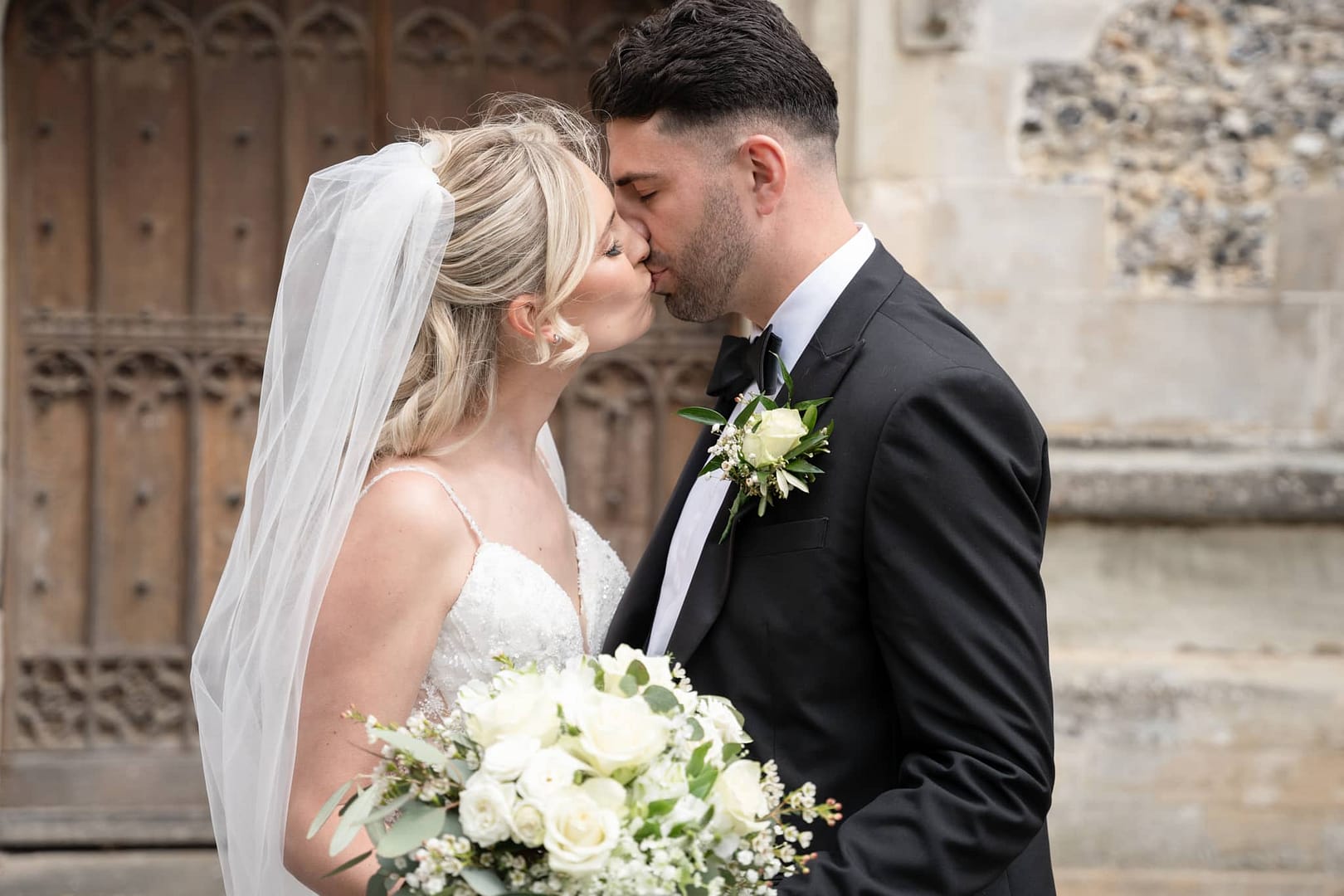 bride and groom kissing by church door