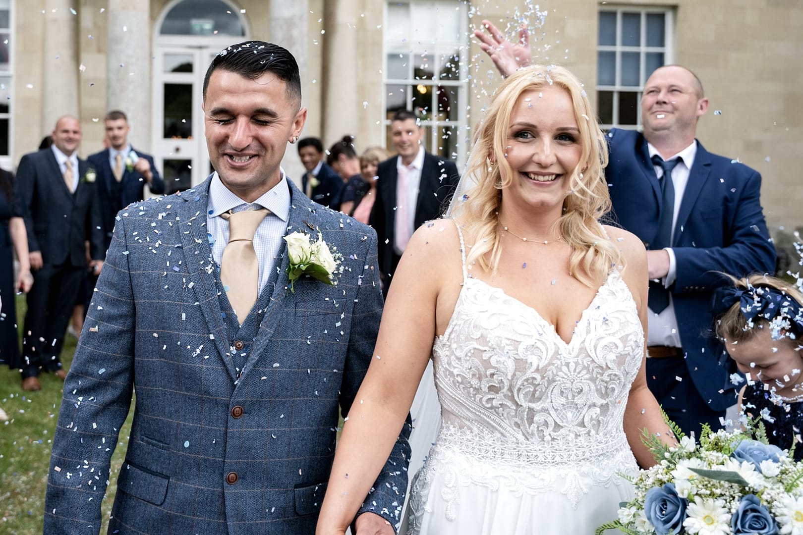 Newlyweds laughing while being covered in a shower of white confetti